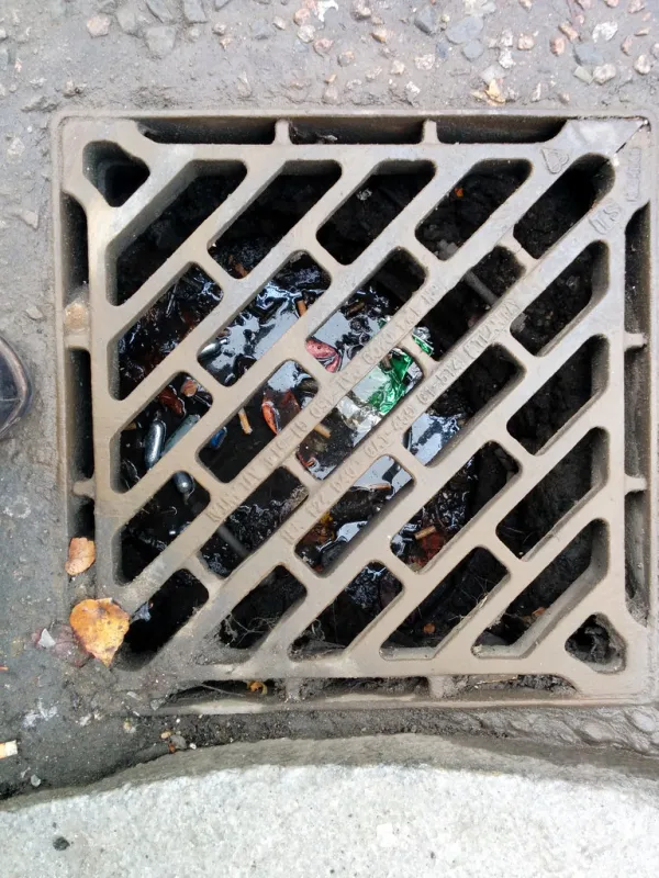 Filthy water, crushed lager tins, nitrous cannisters, ballons, Shoreditch sewer grating, Curtain Road, Hackney, London, UK